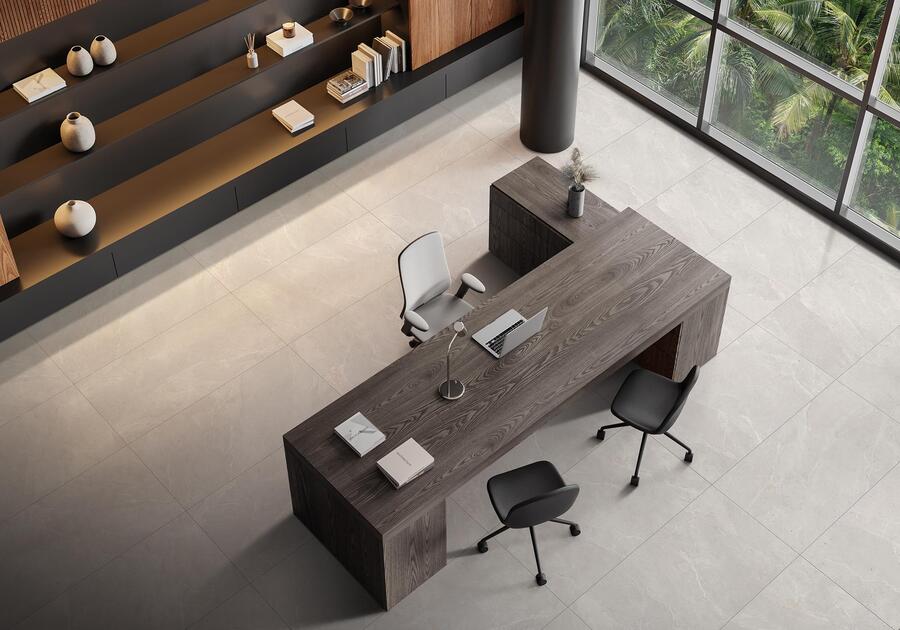 on voit un grand bureau en bois avec du carrelage imitation ardoise au sol. Au fond des étagères bois et noir qui font bibliothèque et une grande baie vitrée avec de la végétation dehors